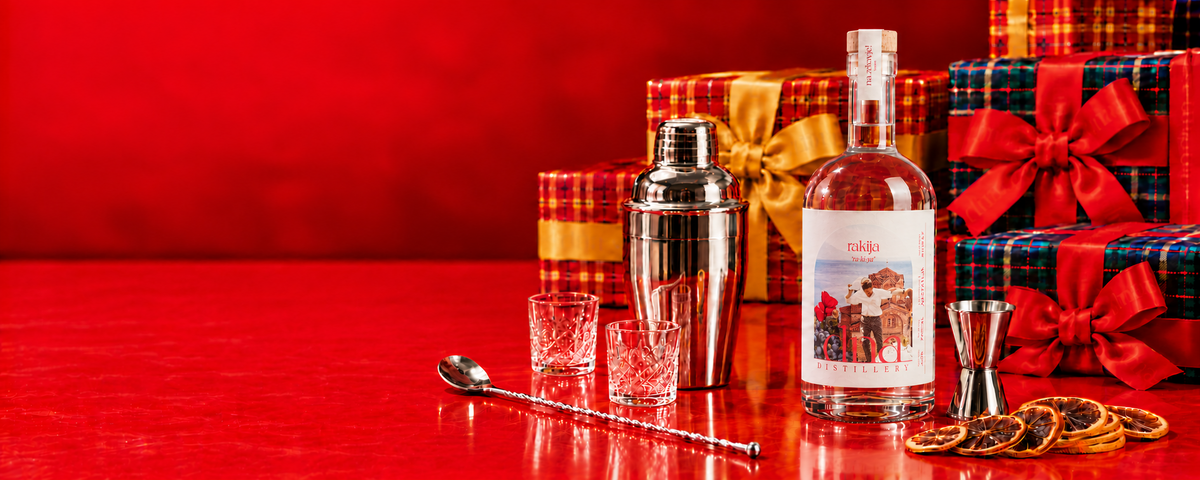 Classic rakija with silver cocktail tools and tartan Christmas gifts on a red background.