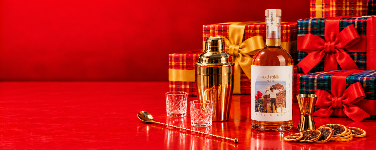 Gold rakija with gold cocktail tools and tartan Christmas gifts on a red background.